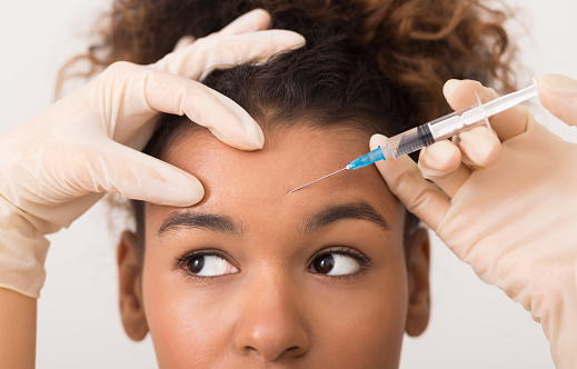 Cosmetic procedures. African-american woman getting botox injection in forehead